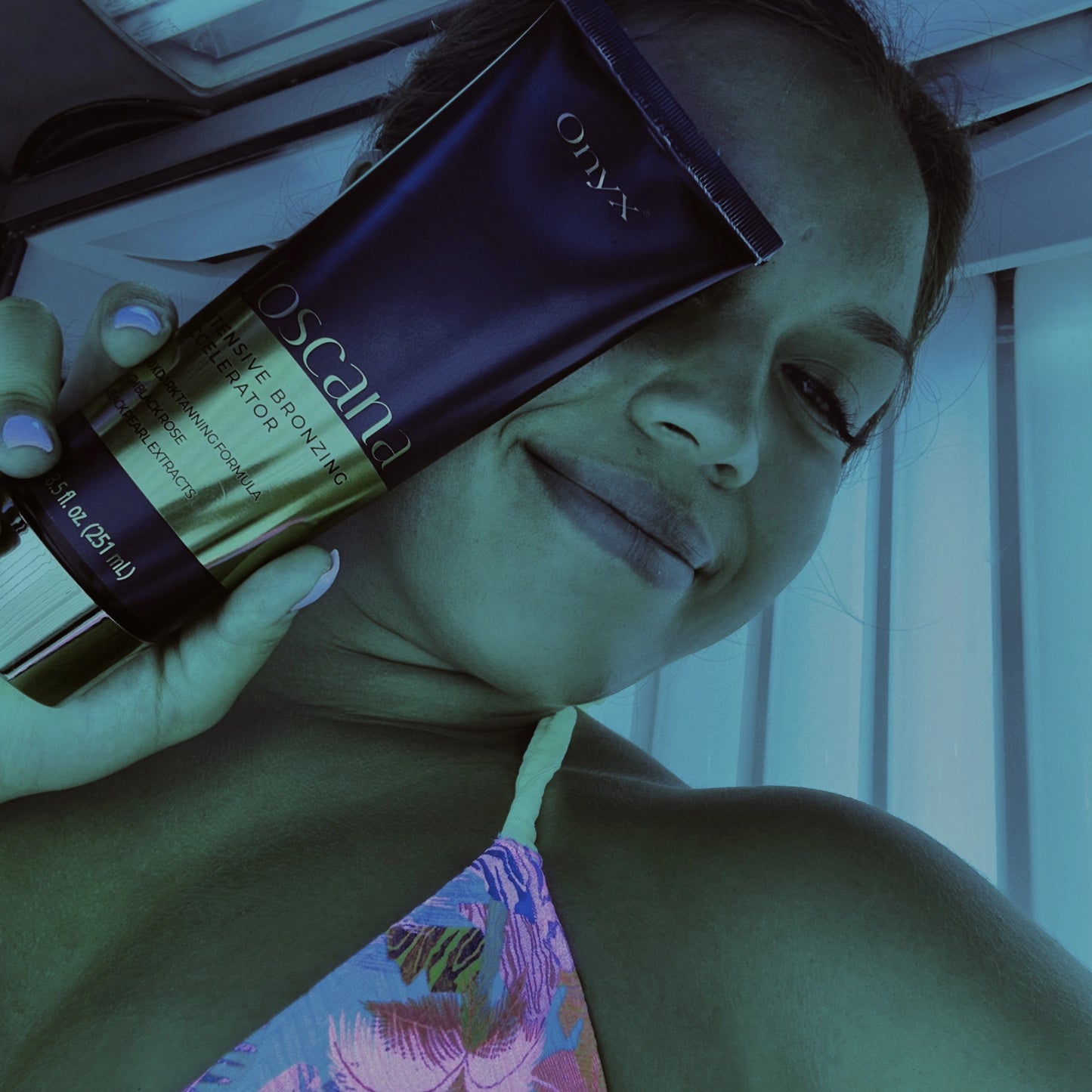 A smiling woman holds up Toscana tanning lotion while tanning indoors.