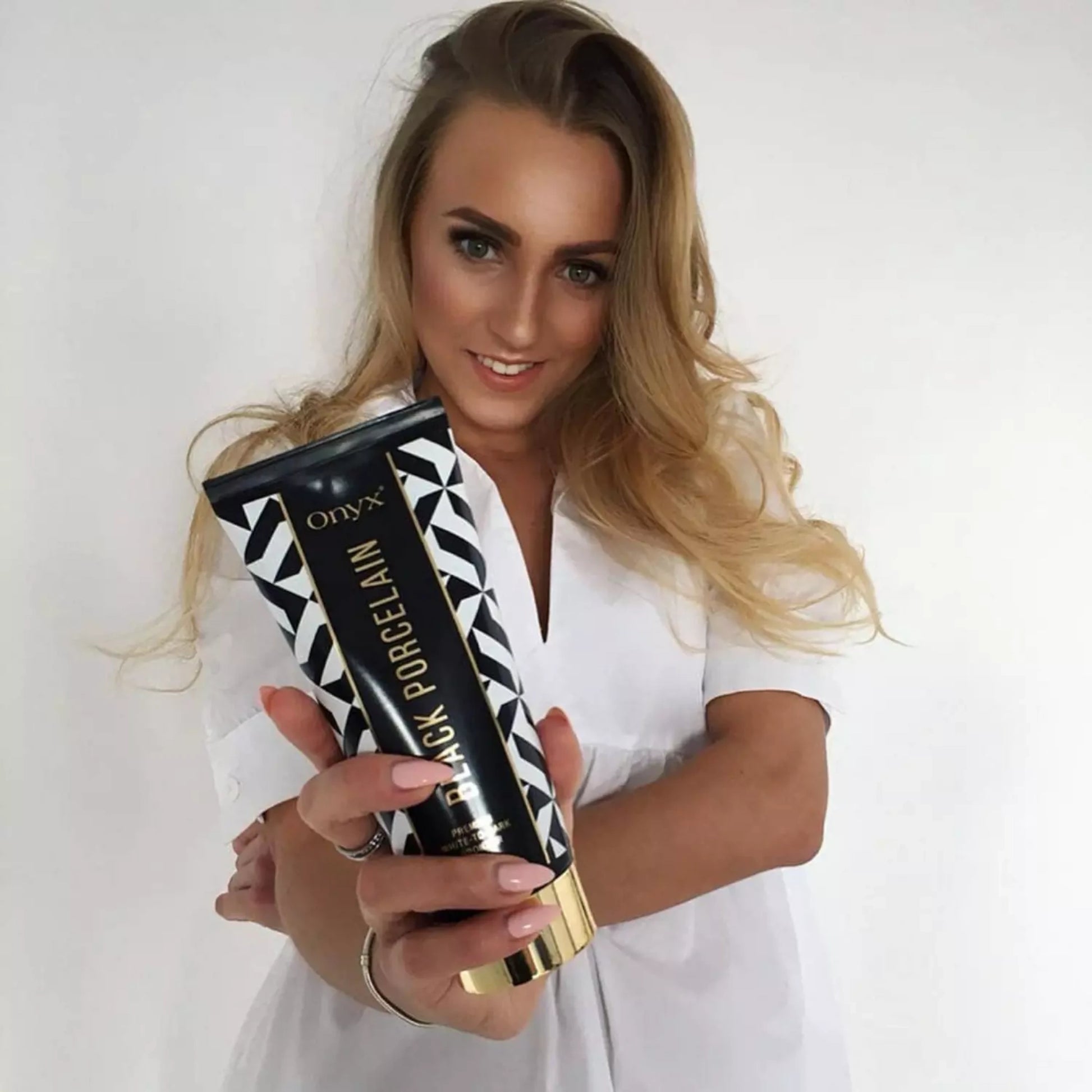 Smiling woman holding Onyx Black Porcelain White-to-Dark Bronzer, showcasing the product’s premium design and tanning benefits.