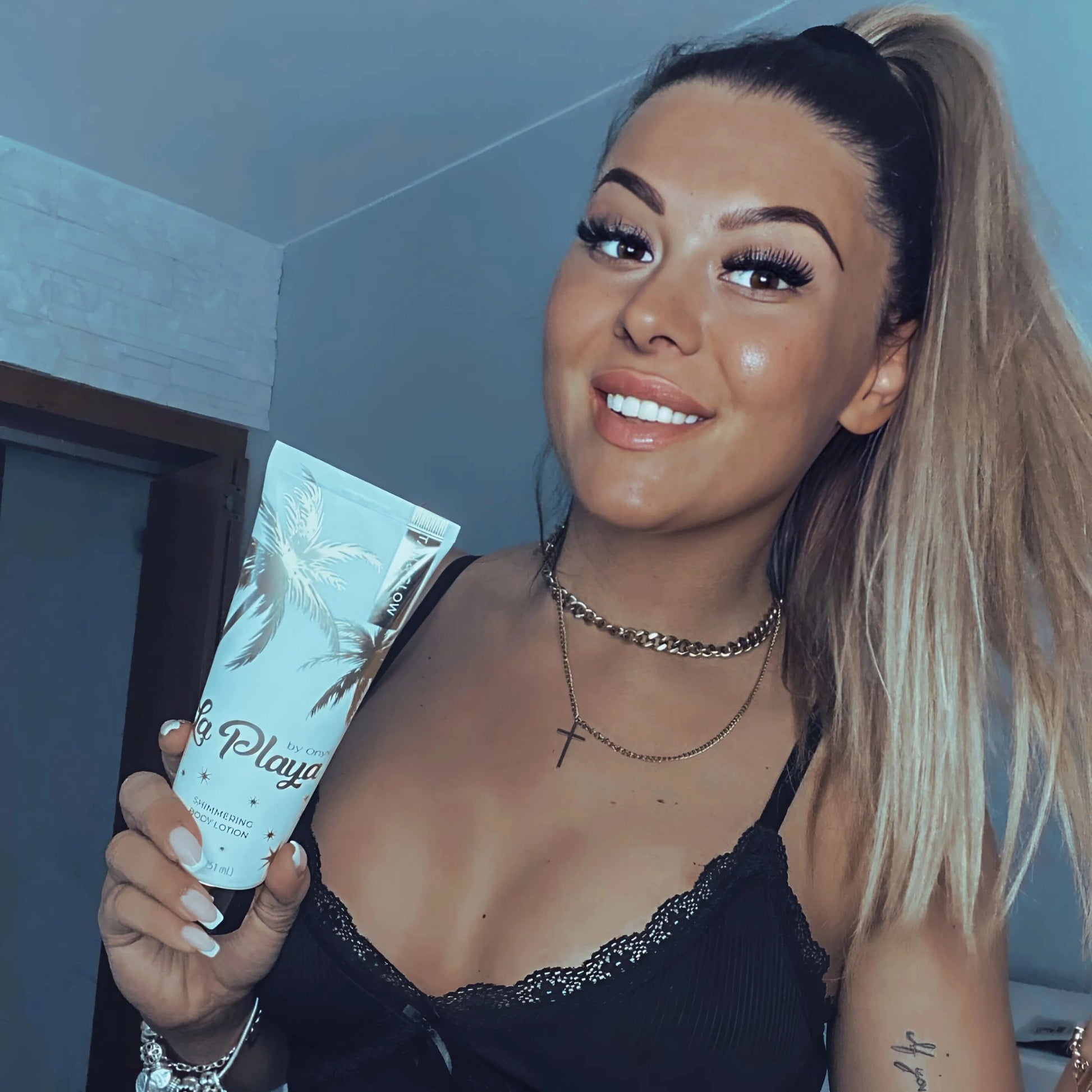 Smiling woman holding Onyx La Playa shimmering lotion, emphasizing post-tan hydration and glow.