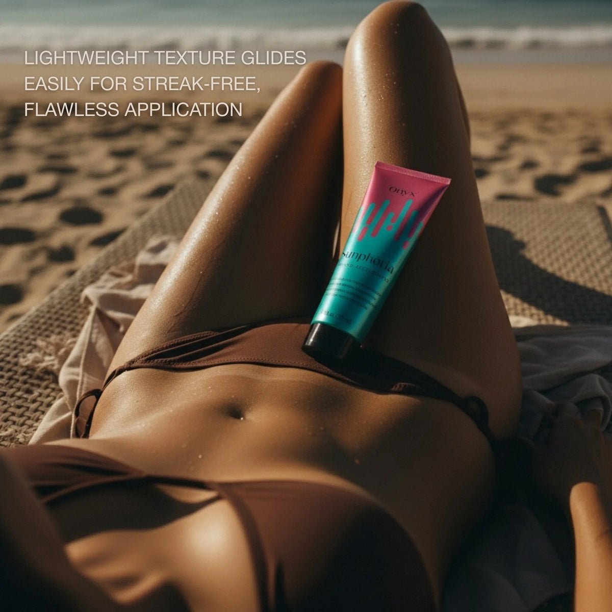 Woman lying on beach with Onyx Sunphoria tanning accelerator bottle placed against her leg near ocean