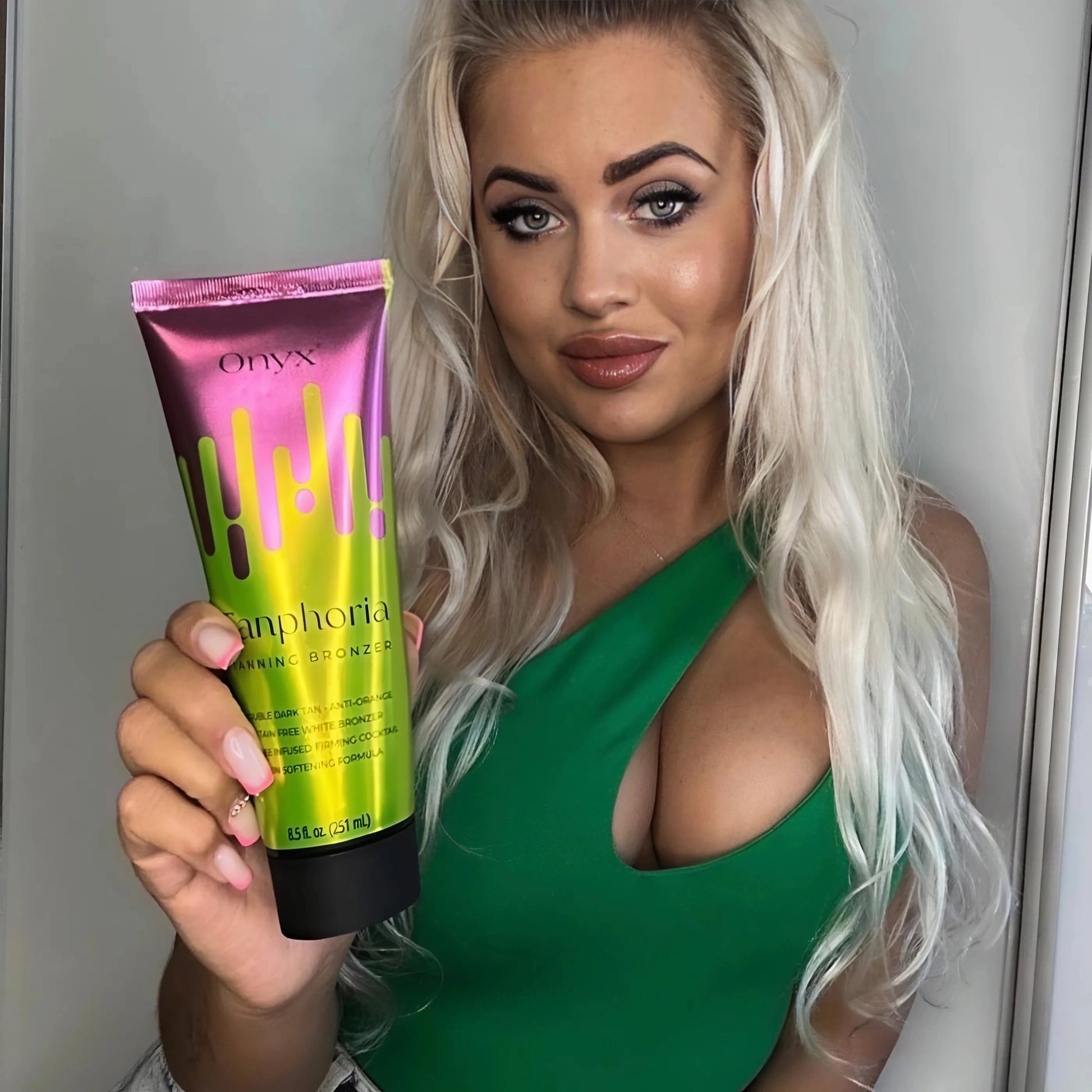 A blonde woman in a green dress holding Onyx Tanphoria Bronzer Lotion, designed for deep tanning.
