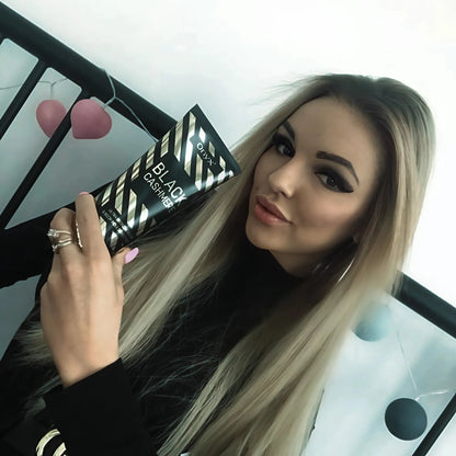 A woman holding Onyx Black Cashmere tanning lotion indoors, with the black and gold product packaging visible near her face.