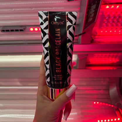 Woman in a swimsuit holding Onyx Black Porcelain White-to-Dark Bronzer inside a vertical tanning booth, preparing for an indoor tanning session.