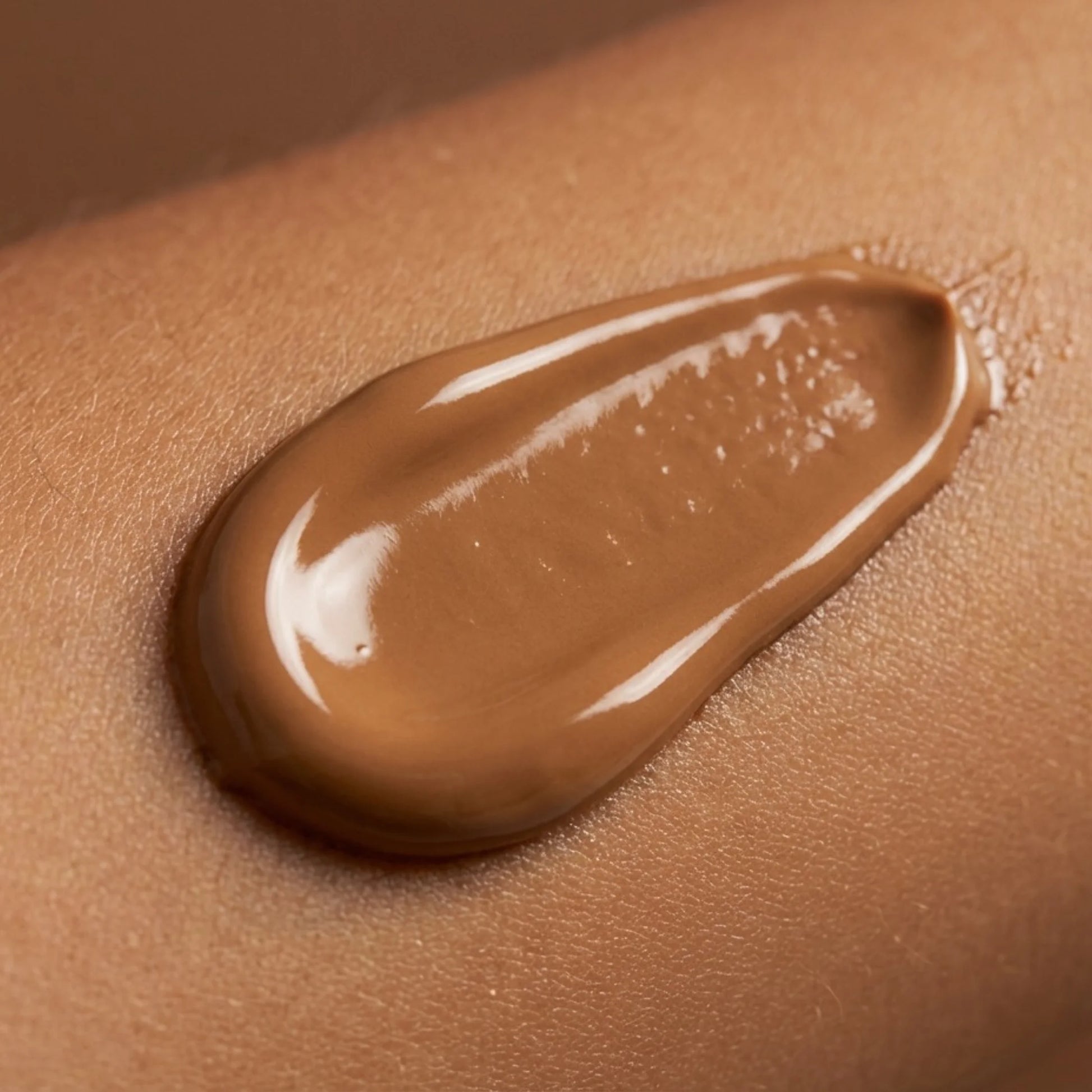 A close-up of brown bronzing tanning lotion texture spread on skin, showing the color and creamy consistency of the formula.
