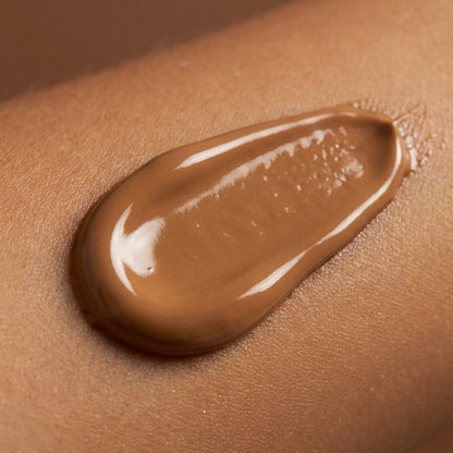 A close-up of brown bronzing tanning lotion texture spread on skin, showing the color and creamy consistency of the formula.
