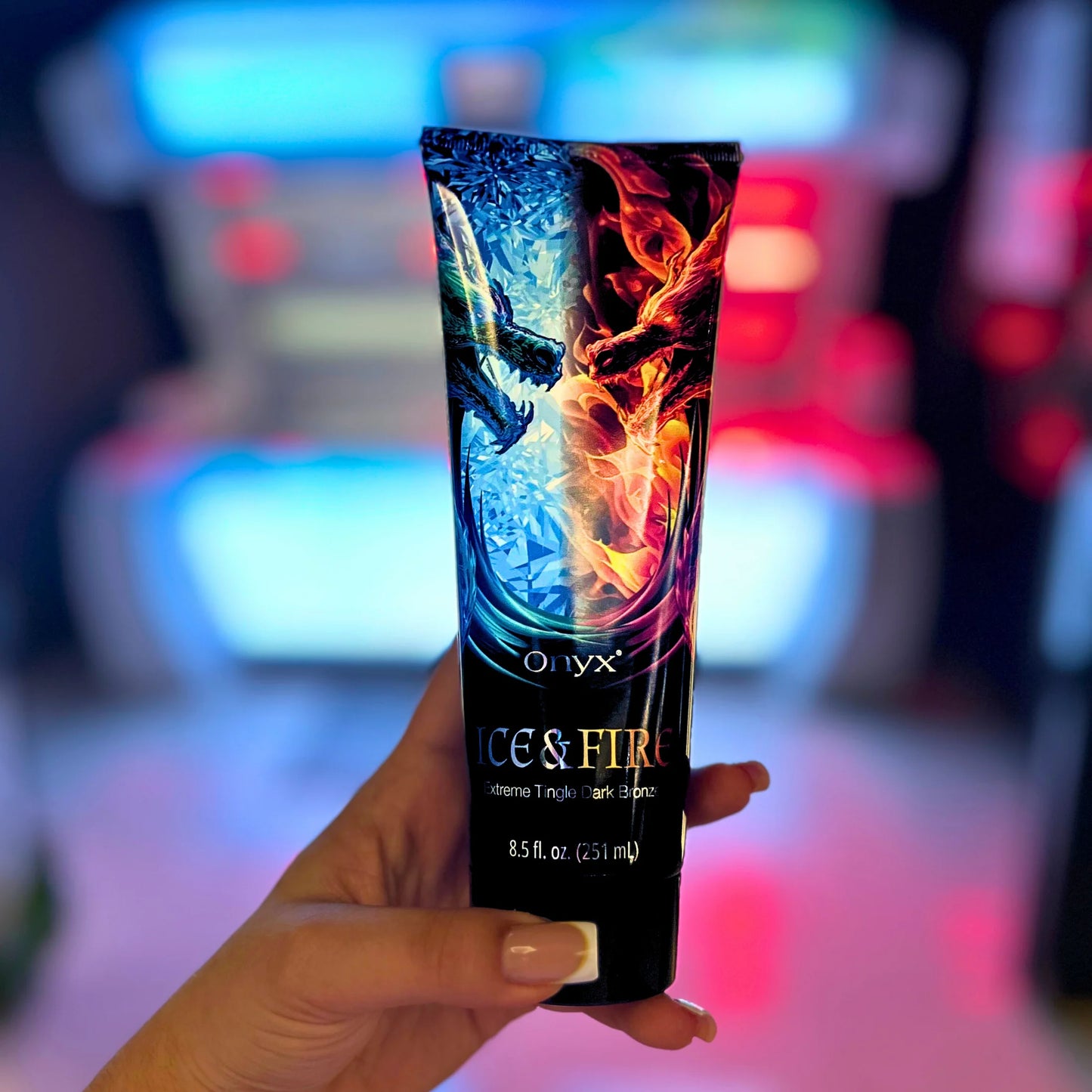 Hand holding Onyx Ice & Fire tanning lotion with blurred indoor background and soft lighting.