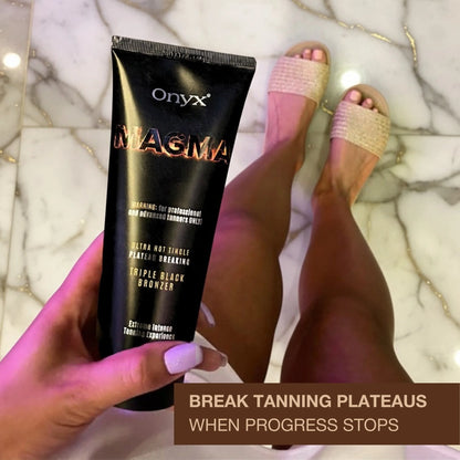 Hand holding Onyx Magma tanning lotion above bronzed legs in casual indoor setting.