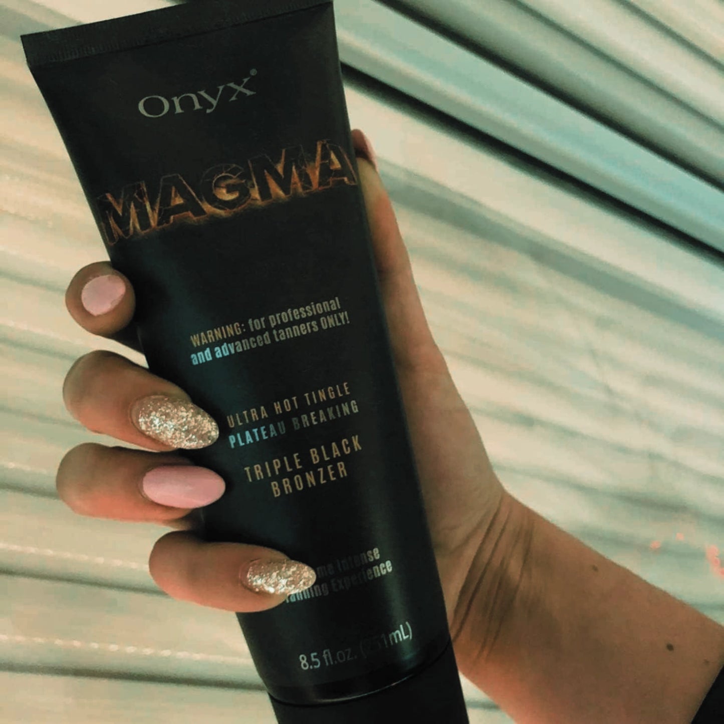 Hand holding Onyx Magma tingle bronzer, ideal for advanced tanners seeking intense color.