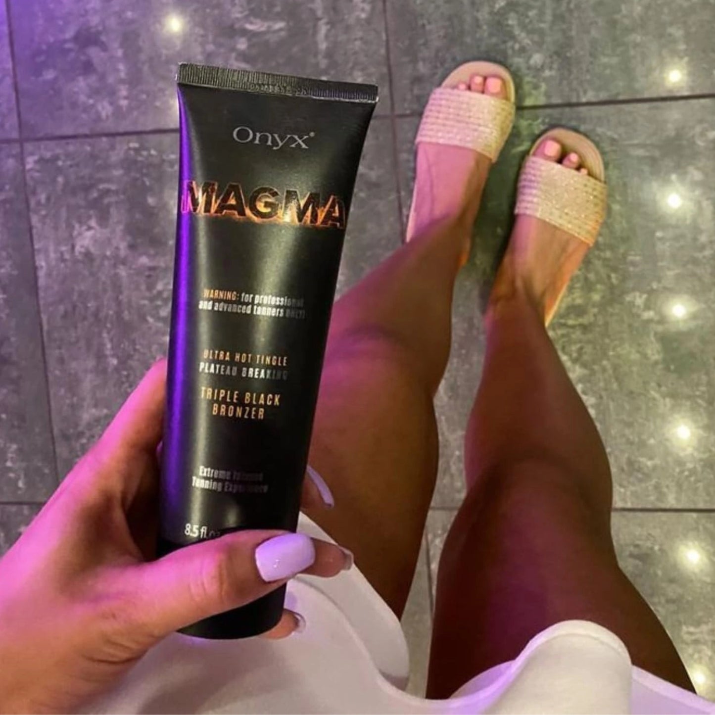 Woman holding Onyx Magma tingle bronzing lotion, showcasing dark and even leg tan.