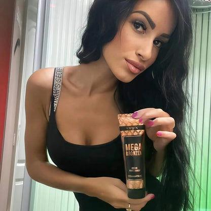Woman holding Onyx Mega Bronzer Tanning Lotion inside a tanning booth – Indoor tanning accelerator for deep, bronzed skin.