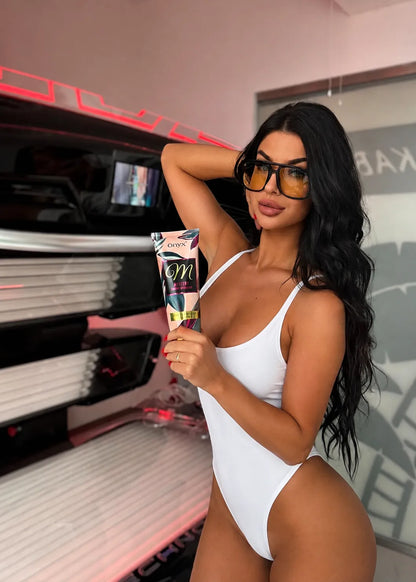 Woman in a white swimsuit holding Onyx Mystery in front of tanning bed