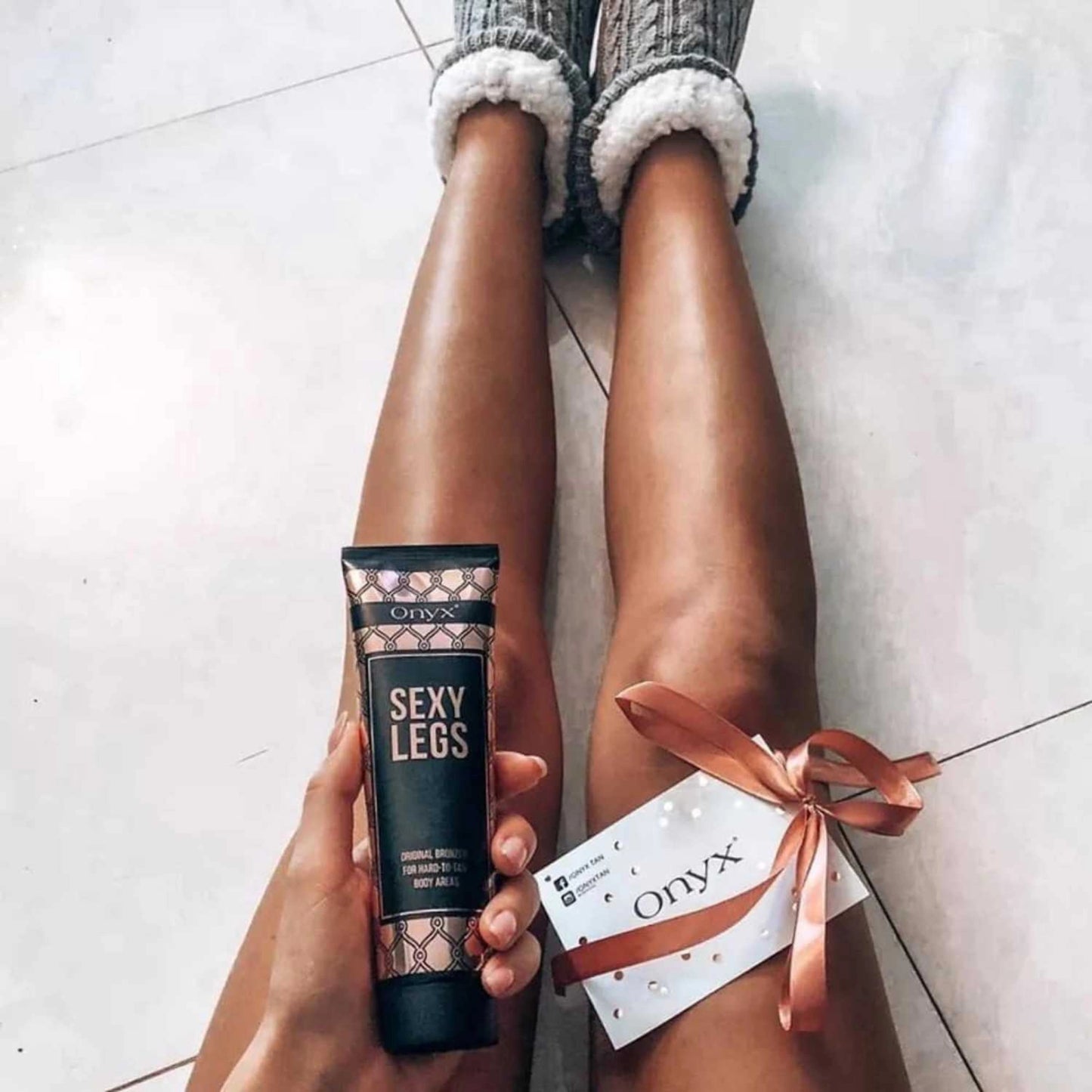 A pair of tanned legs resting on a floor while holding Onyx Sexy Legs bronzing lotion, perfect for achieving an ultra-dark tan.