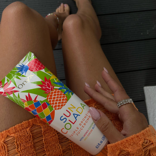 A person holding Onyx SunColada bronzing lotion, showing smooth tanned legs and hydrated skin.