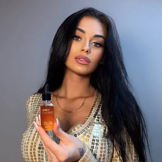 Woman with long dark hair holding a transparent bottle of Onyx Sunl’essence self-tanning drops with orange liquid against a gray background