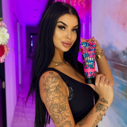 Tattooed woman holding tanning lotion indoors with purple ambient lighting, beauty portrait with detailed arm tattoos.