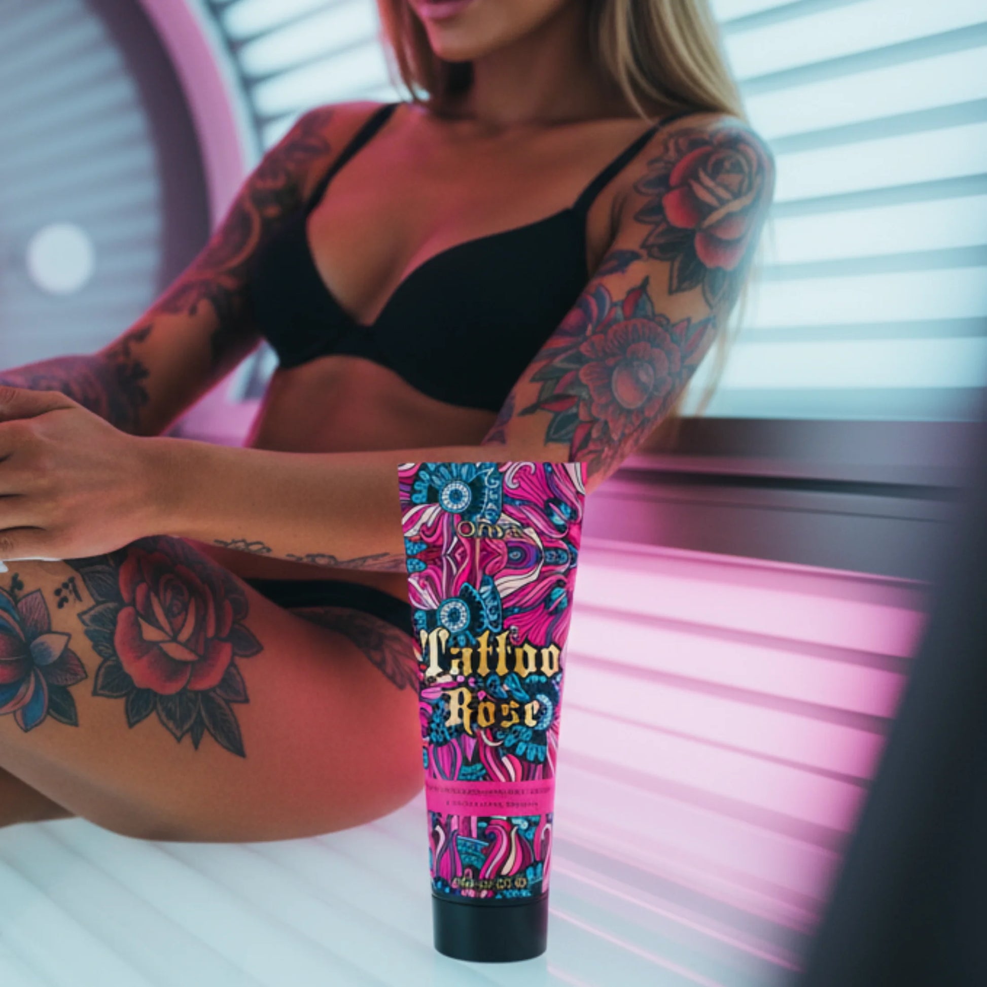 Tanning lotion tube placed in front of tattooed woman sitting in a tanning bed, pink lighting and beauty setup.