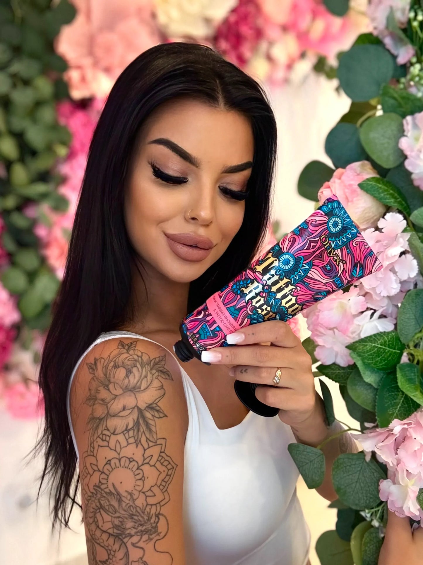 Woman applying Onyx Tattoo Rose tanning lotion with floral and greenery background