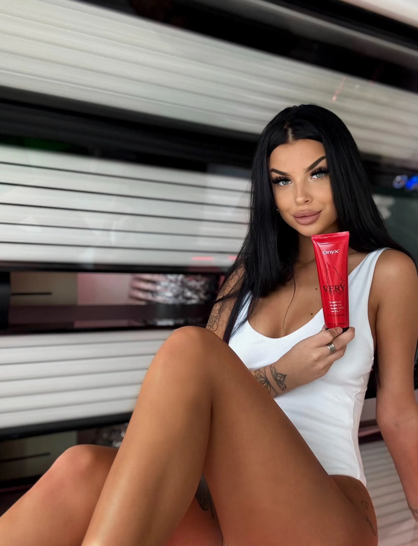Woman holding Onyx Very Sexy Legs tingle tanning lotion in a tanning bed