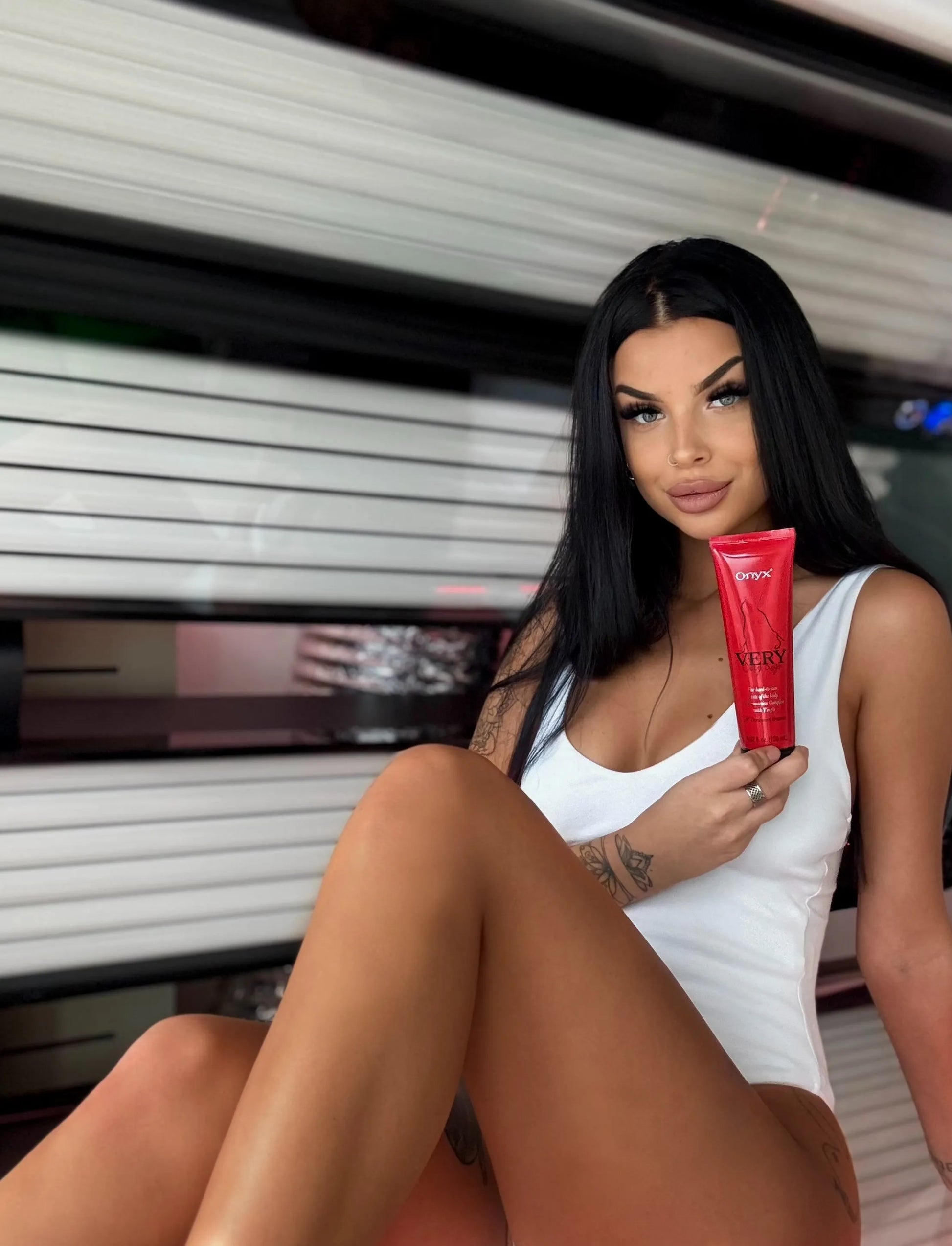 Woman holding Onyx Very Sexy Legs tingle tanning lotion in a tanning bed