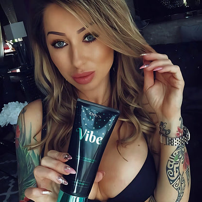 Close-up of Onyx Vibe Tanning Accelerator held by a model with tattooed arms.